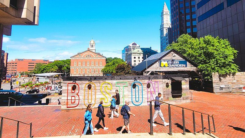 Six people walking past wall with colorful outline letters that spell Boston